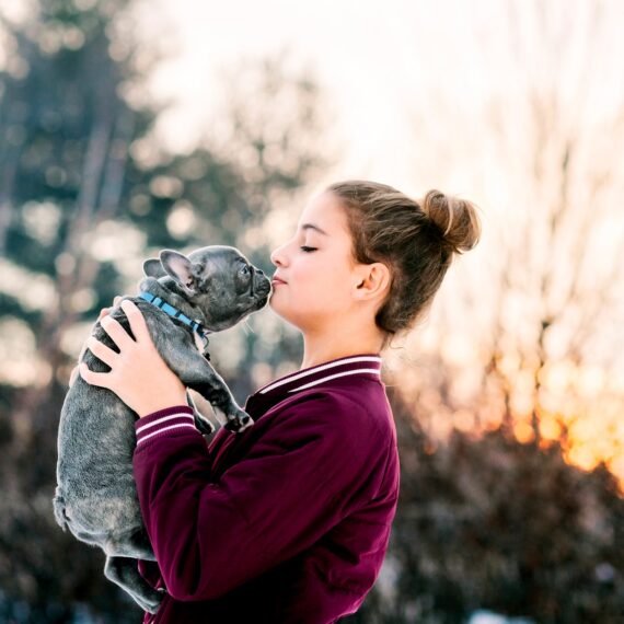 Girl kissing french bulldog puppy outdoors