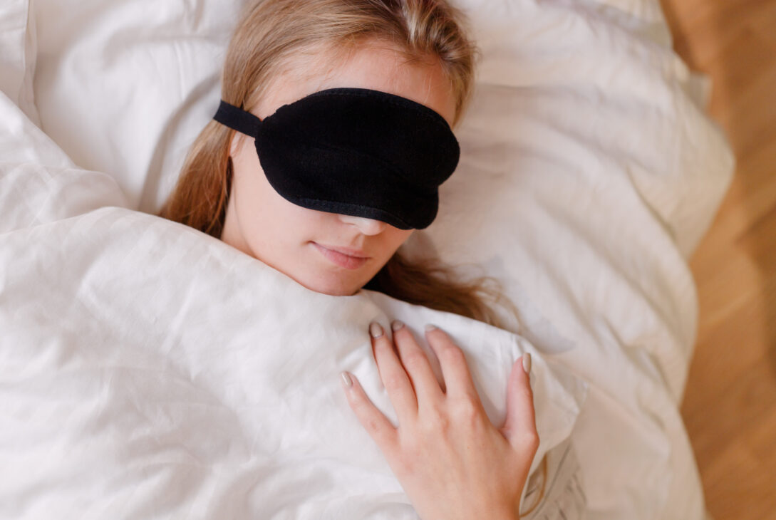 Portrait of beautiful blonde girl with sleeping mask, on white bedclothes