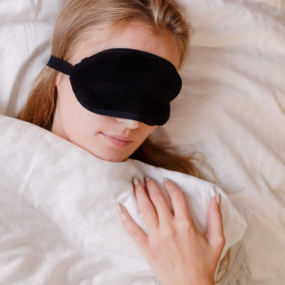 Portrait of beautiful blonde girl with sleeping mask, on white bedclothes